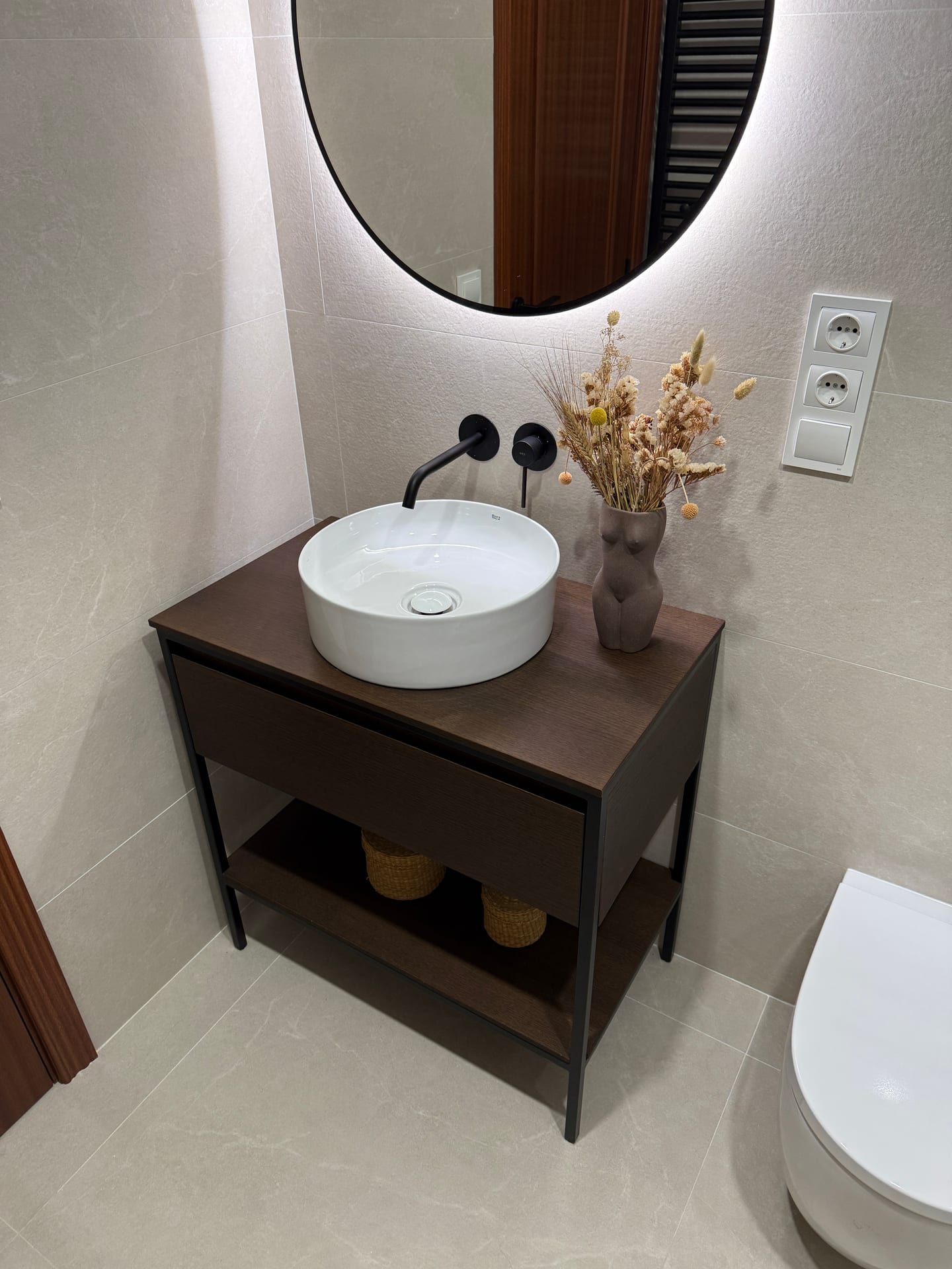 Lavabo sobre encimera con grifería negra y espejo circular retroiluminado