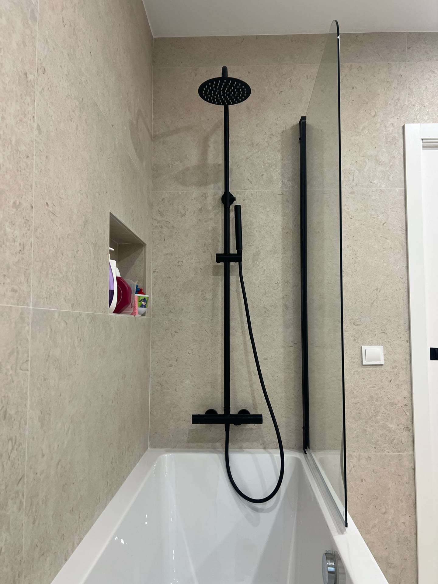 Bañera con columna de ducha en negro mate, mampara de vidrio y hornacina