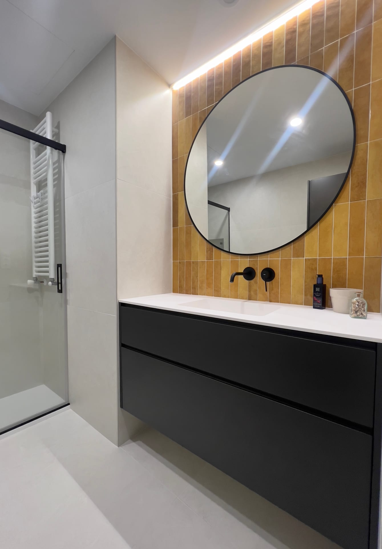 Baño con frente cerámico mostaza, mueble negro y ducha con mampara