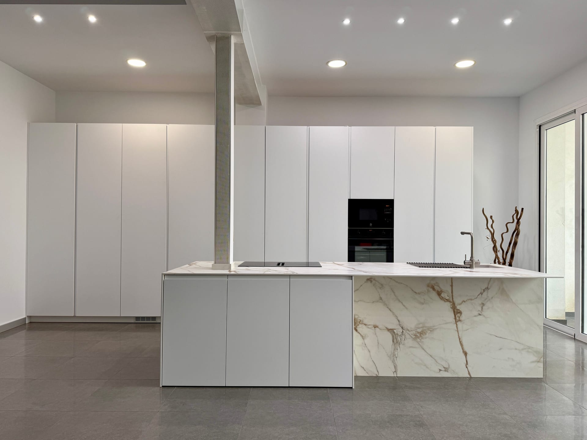 Cocina abierta al salón con isla de Calacatta Gold y frentes blancos
