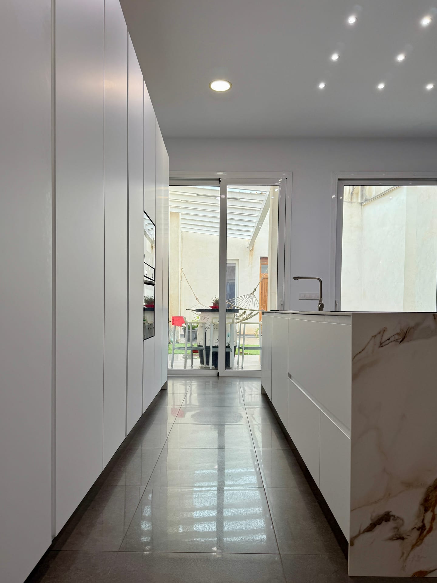 Vista de la cocina hacia el patio, con frentes blancos y suelo porcelánico