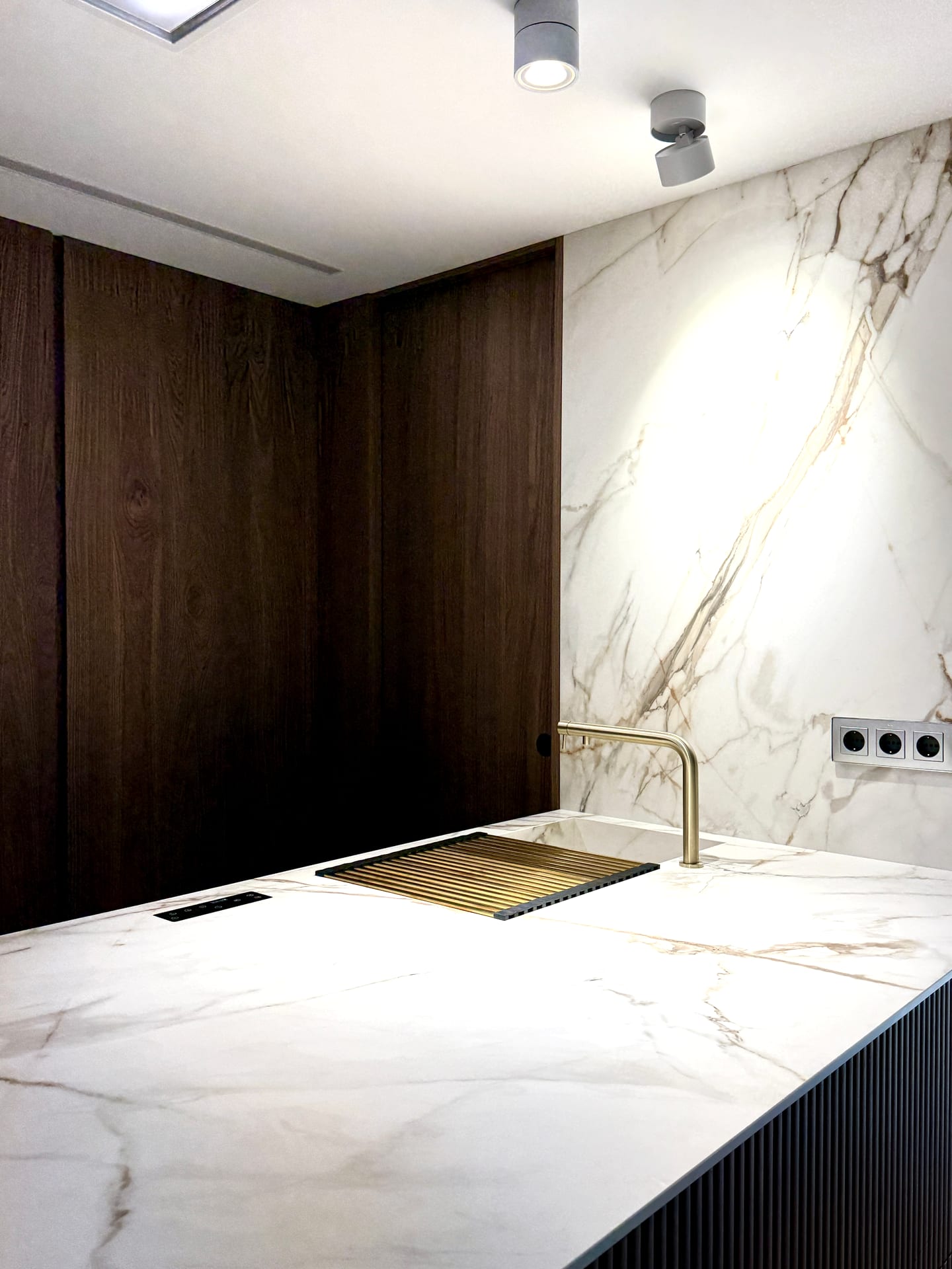 Fregadero integrado en la encimera con grifería dorada y pared de porcelánico efecto mármol