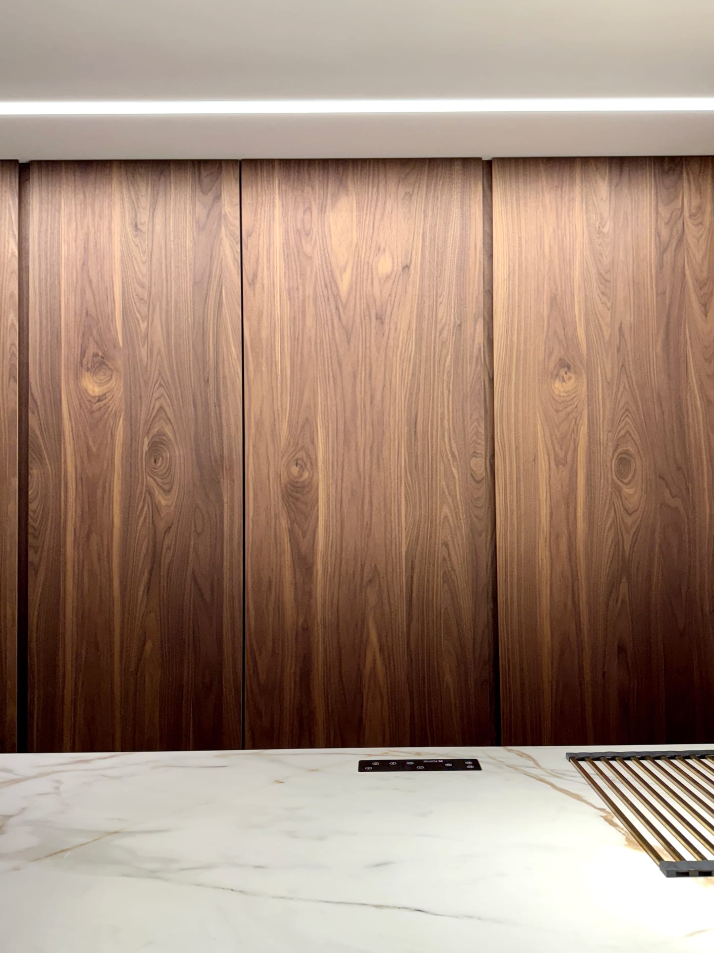 Pared de nogal que oculta toda la cocina, con encimera de Calacatta Gold