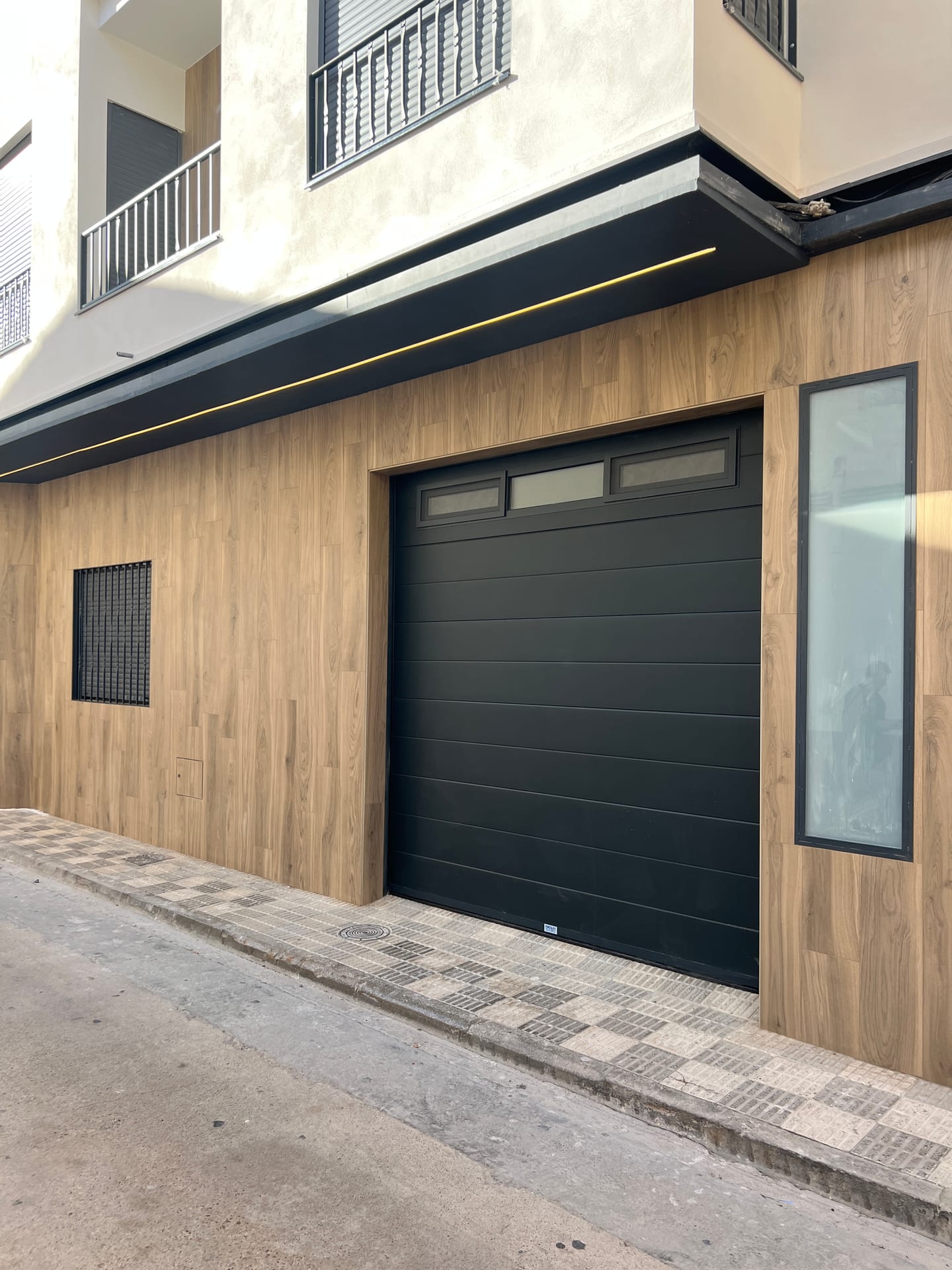 Detalle de la fachada con puerta de garaje negra y revestimiento efecto madera
