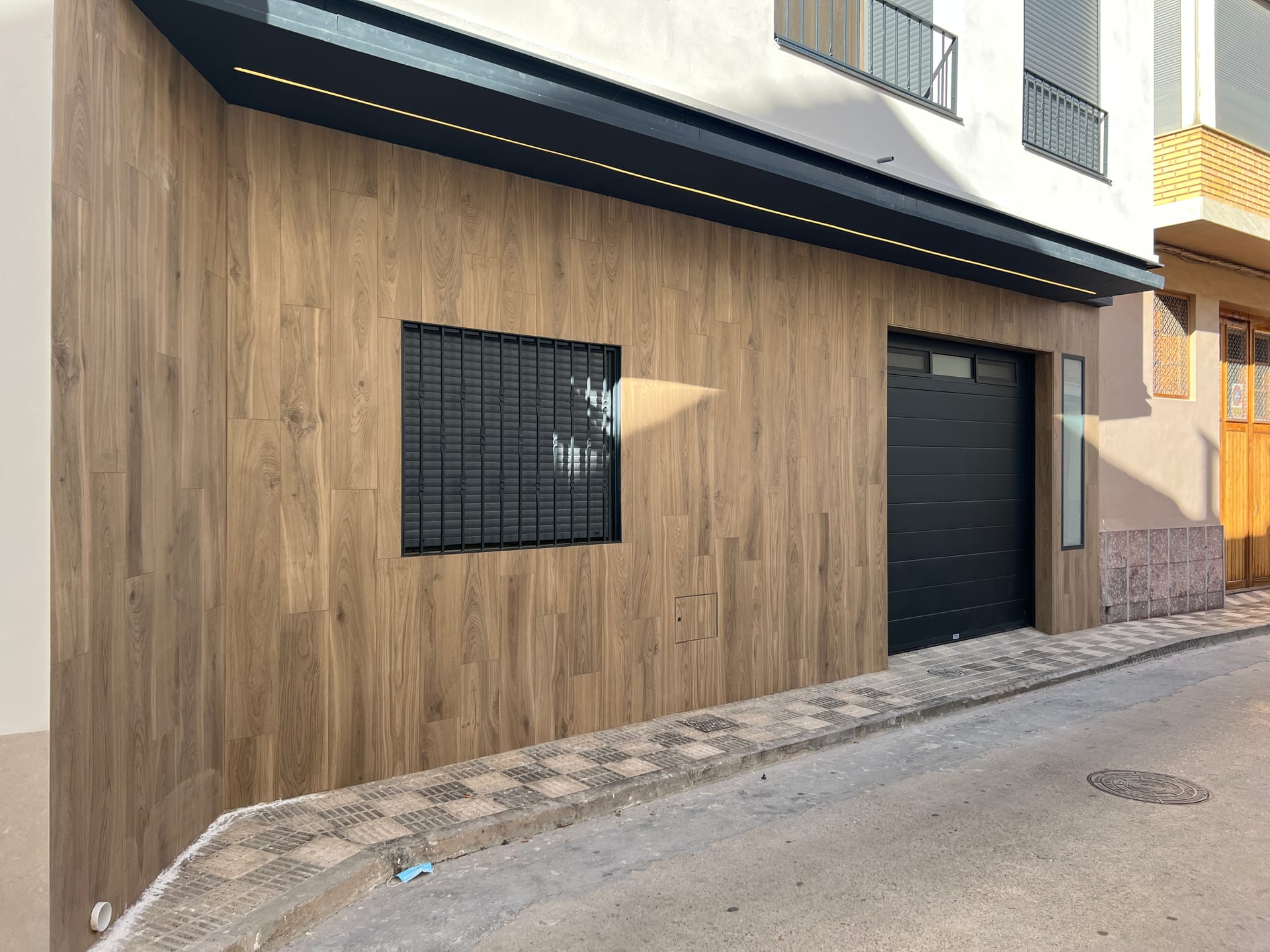 Fachada rehabilitada con revestimiento porcelánico efecto madera y alero negro con LED