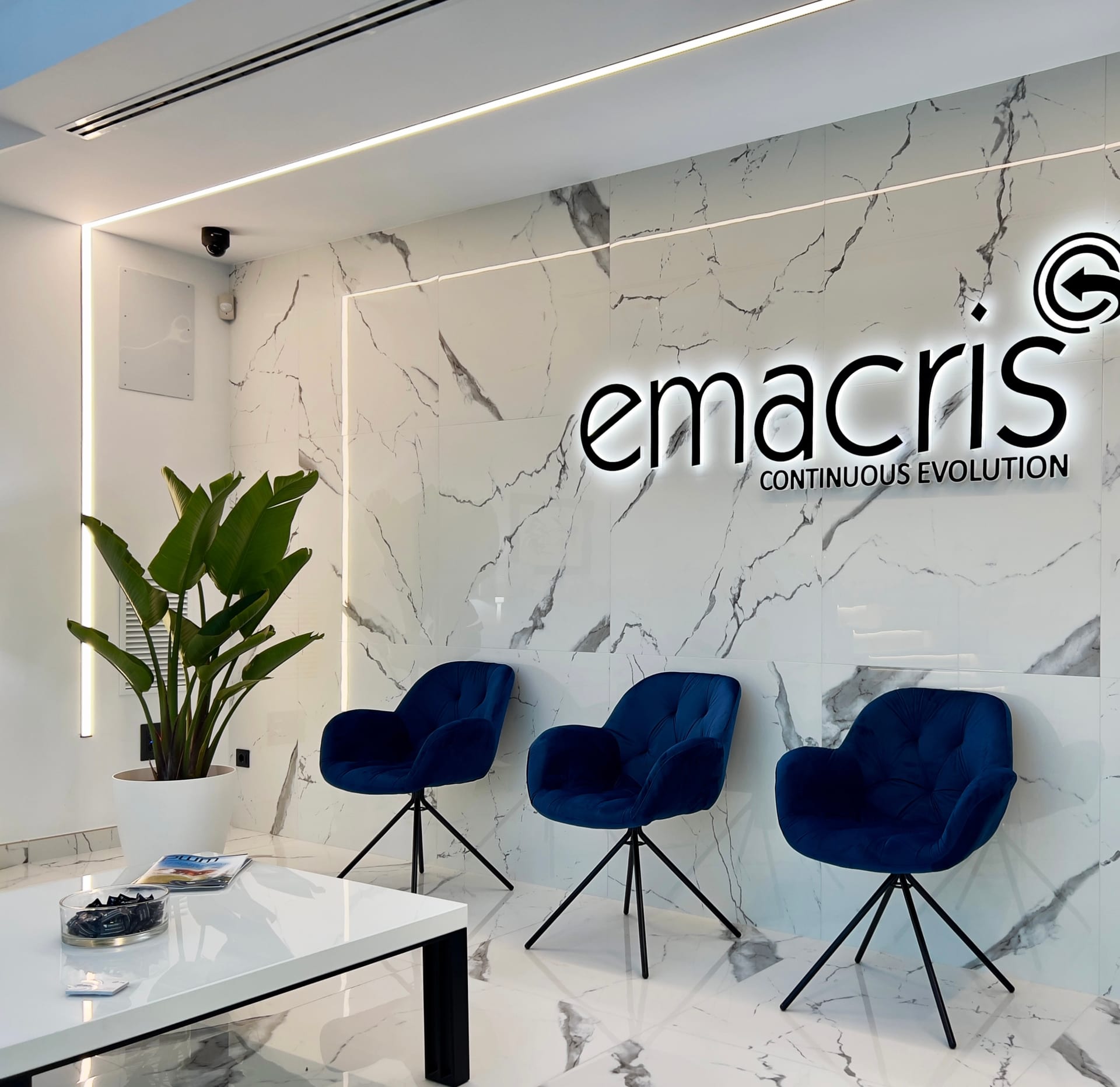 Zona de espera con logotipo retroiluminado sobre pared de mármol y butacas azules