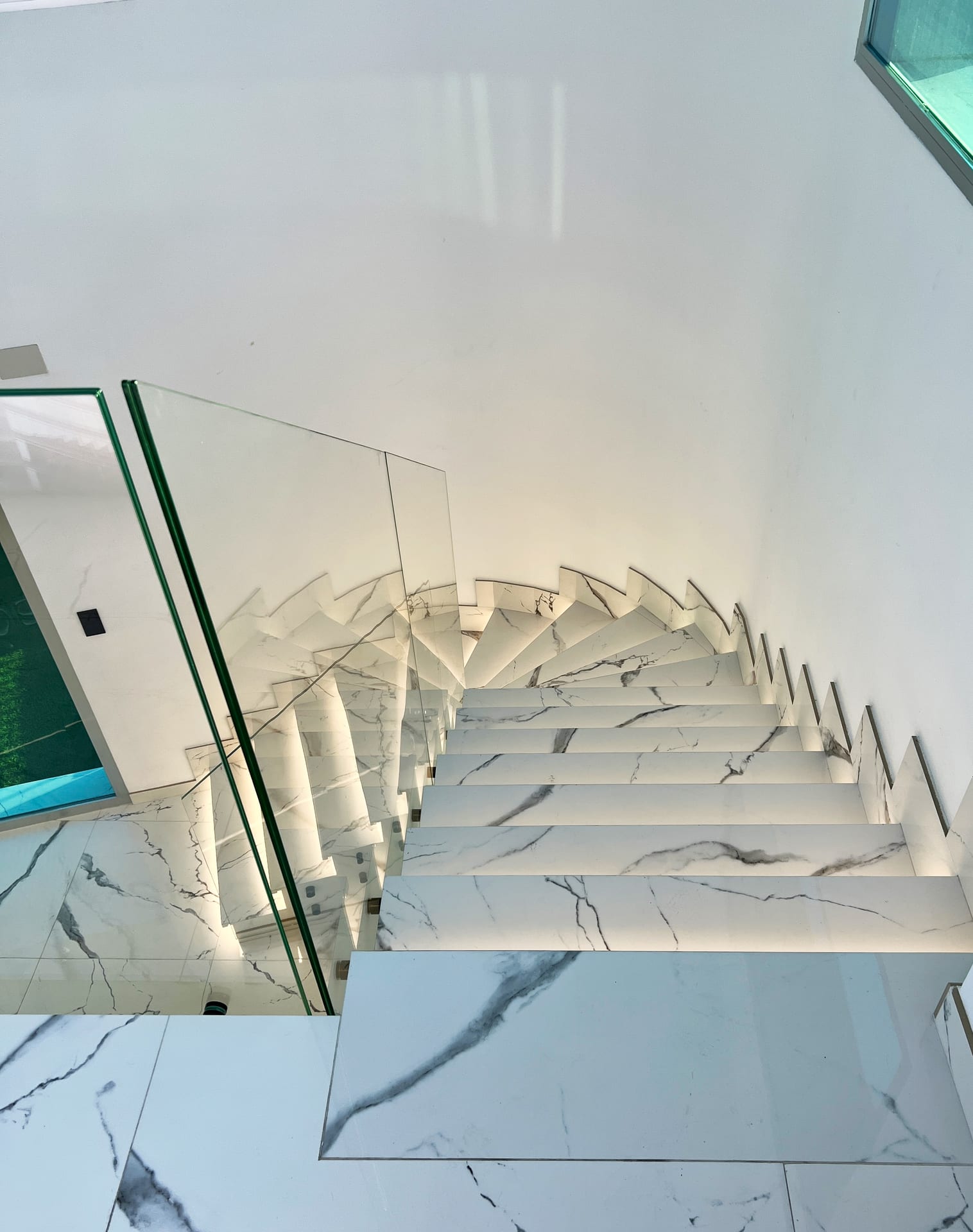 Escalera de mármol vista desde arriba, con barandilla de vidrio