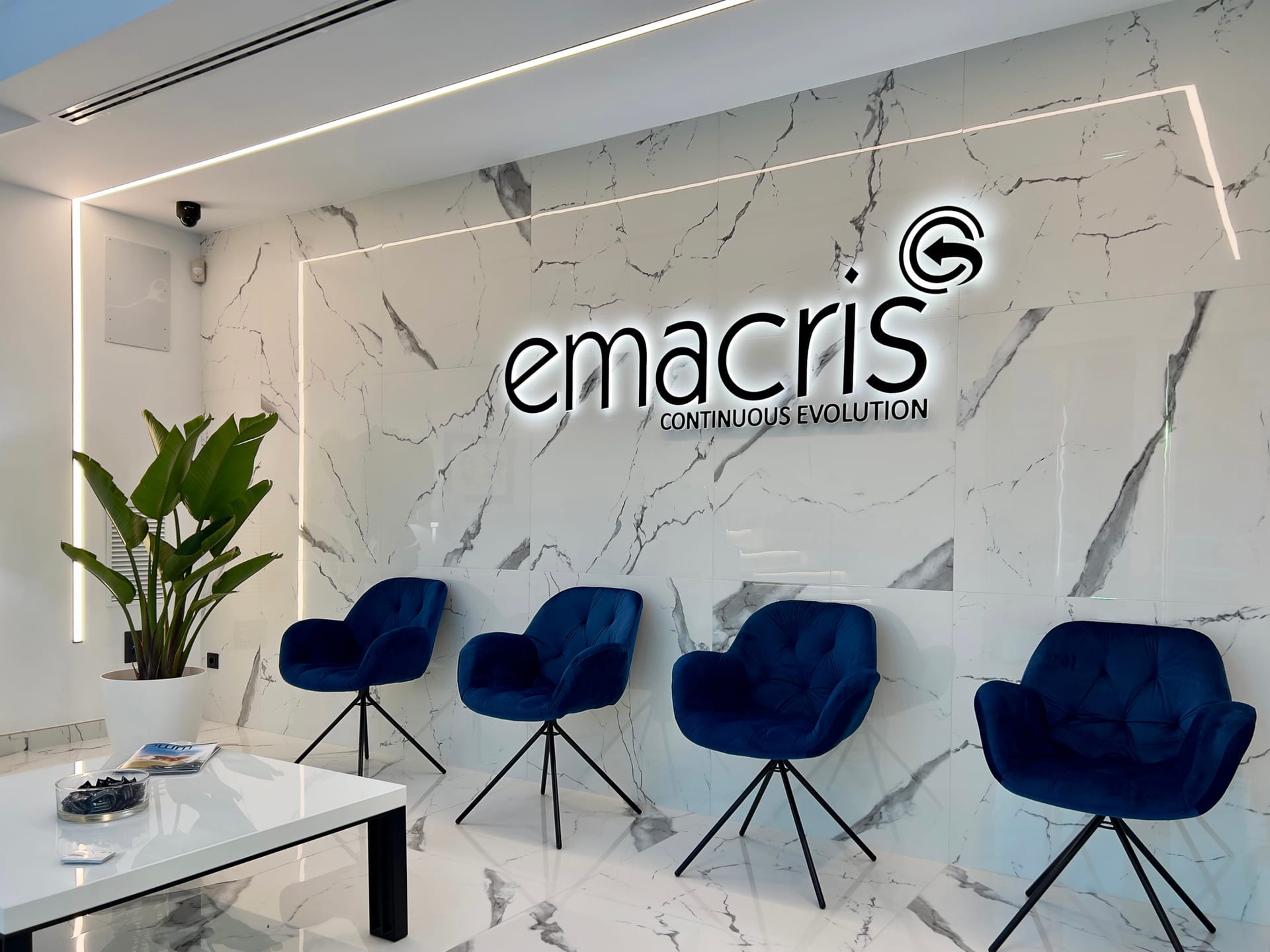 Sala de espera con logotipo corporativo, butacas azules y vegetación