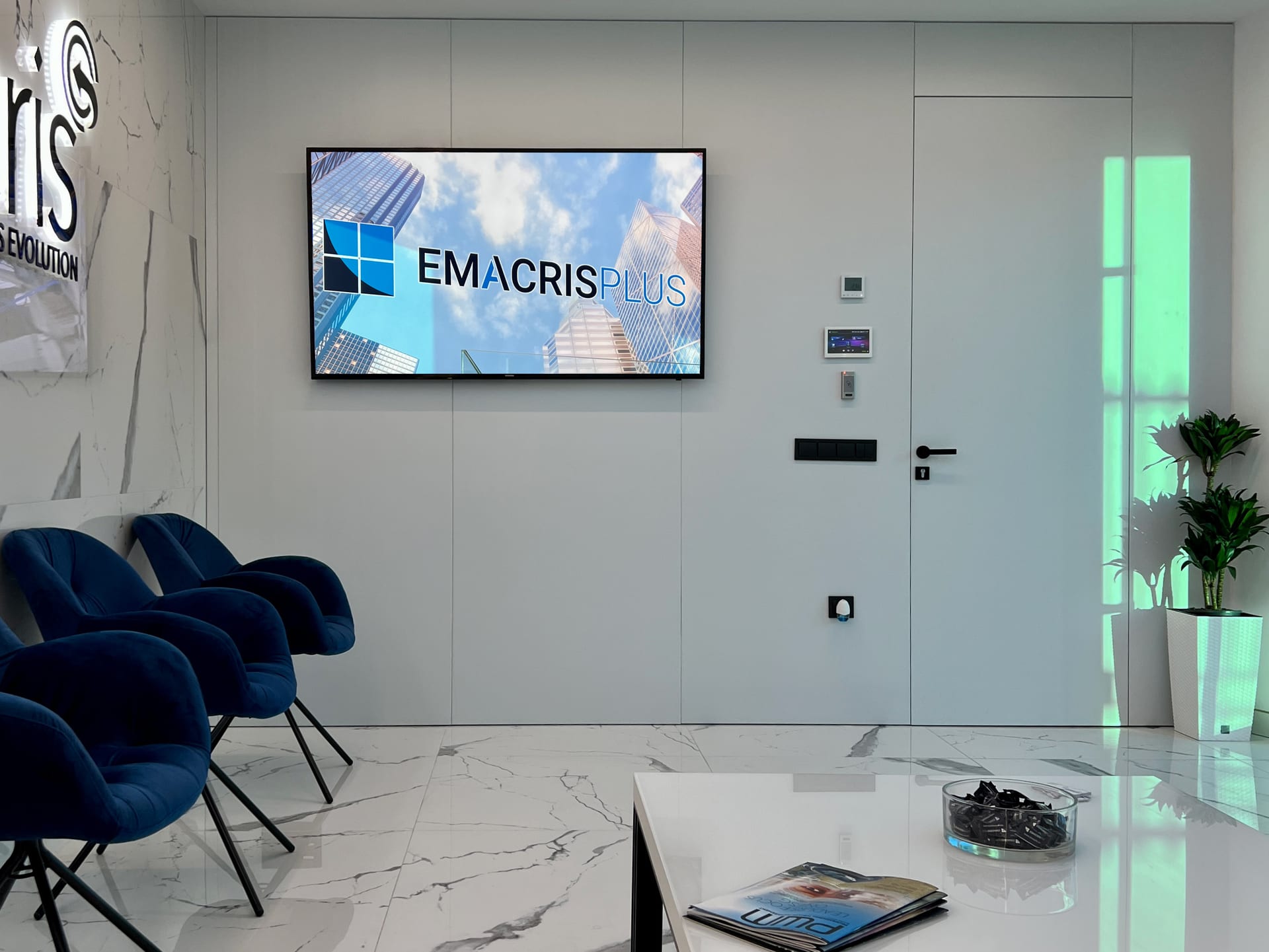 Zona de espera con pantalla corporativa y butacas azules
