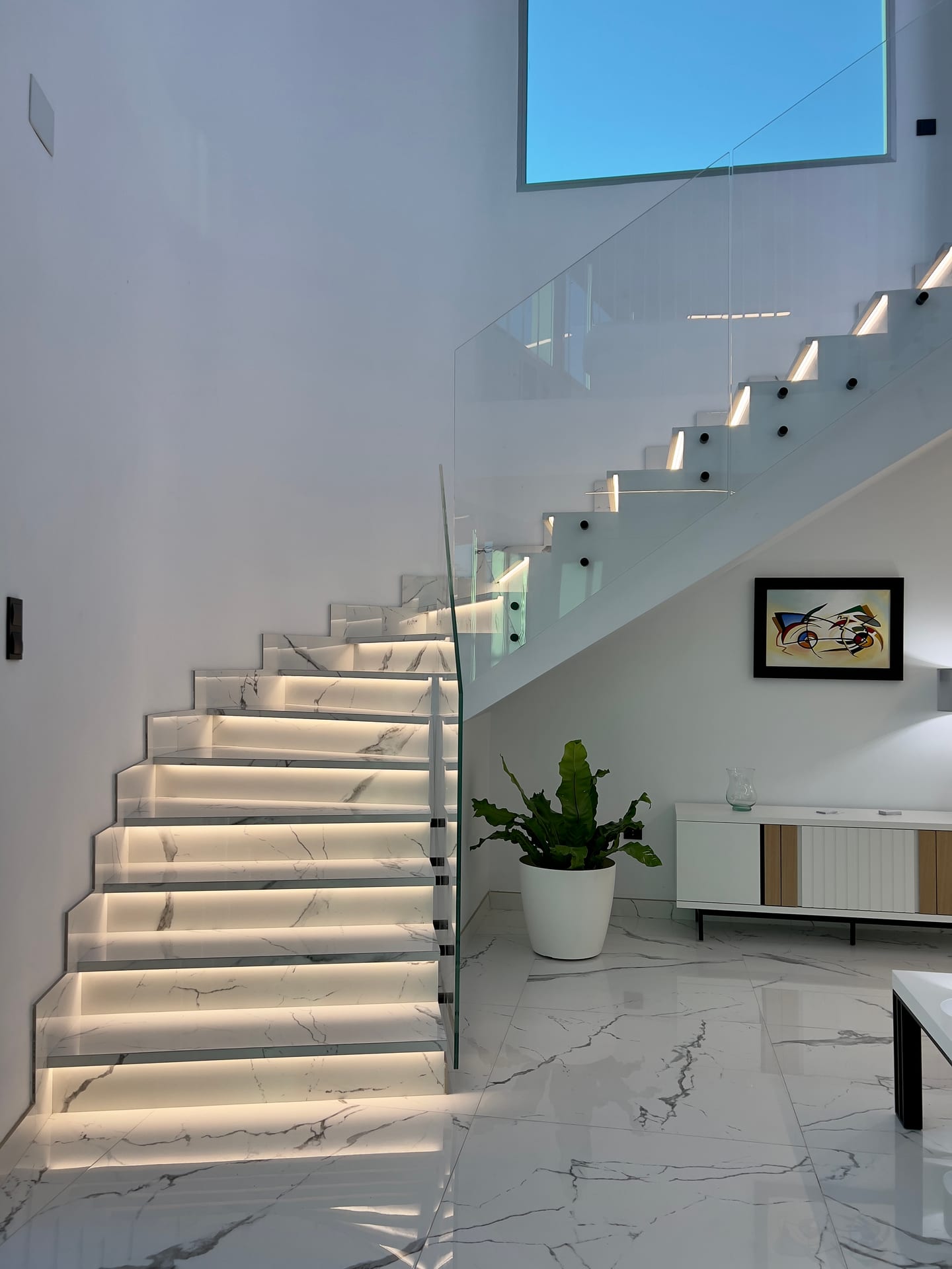 Escalera con peldaños de mármol retroiluminados y barandilla de vidrio