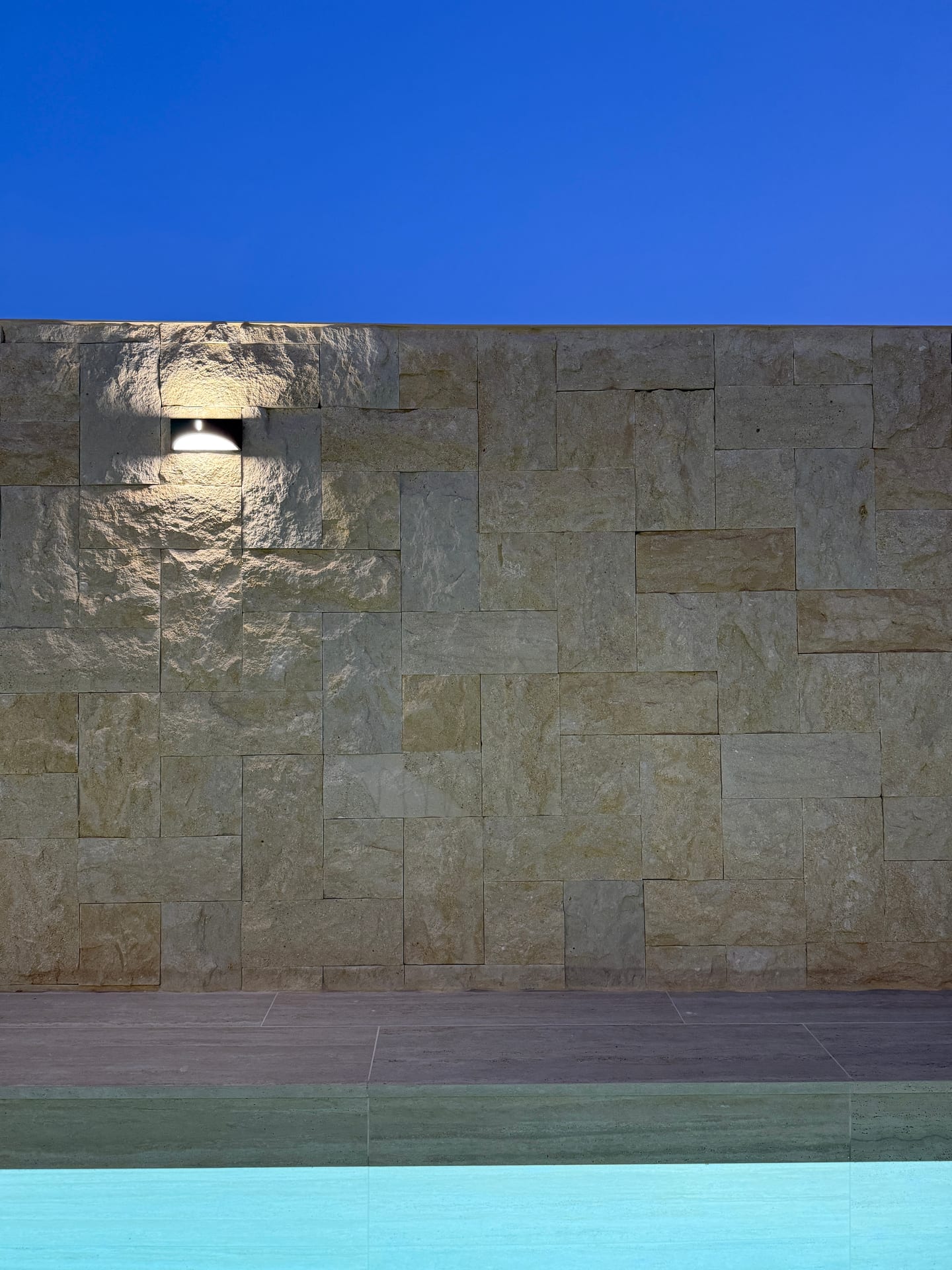 Muro de piedra natural iluminado junto a la lámina de agua de la piscina